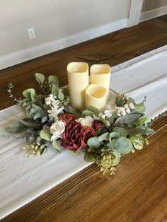 two candles sitting on top of a table with flowers and greenery around the edges