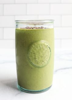 a green smoothie in a mason jar on a marble counter with white tiles behind it