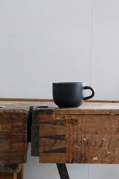 a black coffee cup sitting on top of a wooden table next to a white wall