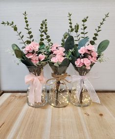 three vases with pink flowers and greenery in them on a wooden table top