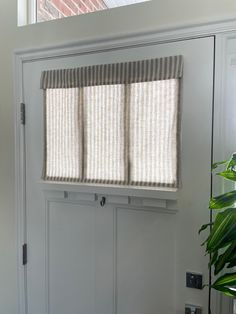 a white front door with three blinds on the windowsill and a potted plant next to it