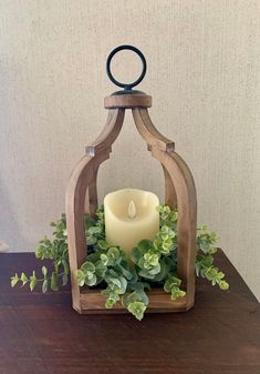 a candle is lit in a wooden lantern holder with greenery on the table next to it