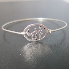 Silver Om Bracelet - A silver tone Om sign has been transformed into an Om bangle bracelet with a silver filled band for you to wear. I can also make this Om bracelet with a sterling silver band for an additional $10. If you would like this option for your Om symbol jewelry, select from options when ordering your Chakra bracelet. This Om stacking bangle looks great together with others from my collection as you can see from the last picture. Have fun stacking your yoga bangle bracelet with other Silver Nickel-free Bangle For Friendship, Adjustable Silver Jubilee Name Bracelet, Silver Metal Friendship Bracelets, Silver Jubilee Bracelet For Friendship, Silver Jubilee Name Bracelet, Silver Round Name Bracelet, Symbolic Sterling Silver Friendship Bracelets, Silver Round Friendship Bracelets, Silver Engraved Bangle For Friendship