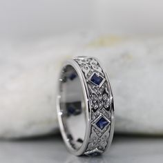 a white gold ring with blue sapphires and diamonds on the side, sitting on a rock