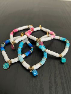 three bracelets with different colored beads and charms on them sitting on a black surface