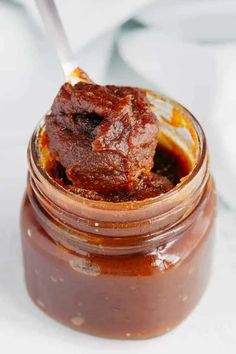 a jar filled with sauce sitting on top of a white table next to a spoon