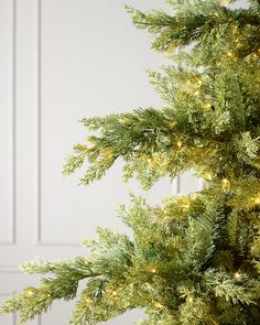 a close up of a christmas tree with lights on the branches and white walls in the background