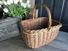 a wicker basket sitting on the ground next to a vase with flowers in it