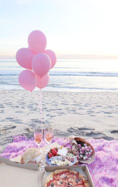 a pizza and some pink balloons on a blanket at the beach with food in front of it