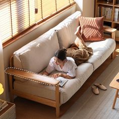 a woman laying on top of a couch in a living room next to a window