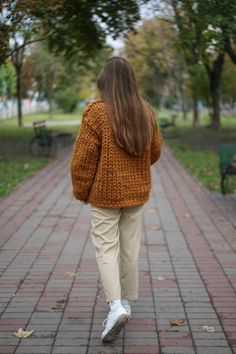 a woman walking down a brick path in a park wearing a brown sweater and khaki pants