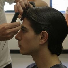 a man getting his hair cut by another man in a room with other people around him