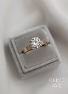 an engagement ring in a velvet box on a white cloth background with the words olive ave written below it