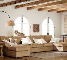 a living room filled with lots of furniture next to two large windows and wooden beams