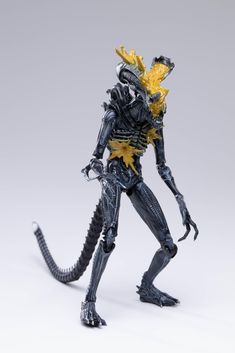 a toy alien is standing with its head turned to the side and arms outstretched, holding a