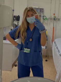 a woman in scrubs and medical gloves is looking at the camera while wearing a face mask