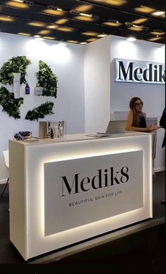 a woman sitting at a desk in front of a medik8 sign on display