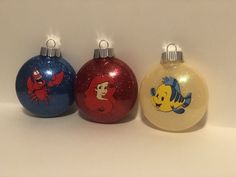 three christmas ornaments with cartoon characters on them are lined up against a white background and one is red, the other blue