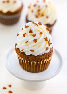 three cupcakes with white frosting and sprinkles on a plate