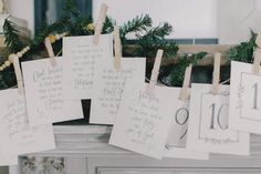 some cards are hanging from clothes pins on a mantle with pine branches and garland around them