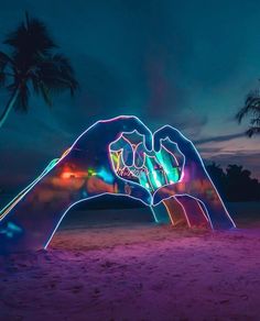 two hands are projected in the sand at night with palm trees and buildings in the background