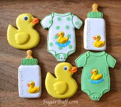 baby shower cookies with rubber ducks and onesuits on wooden table next to bottle