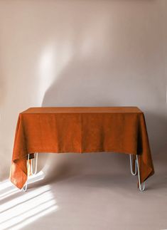 an orange table cloth on a metal stand in front of a white wall with sunlight coming through the window