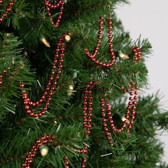 a close up of a christmas tree with red beads on it's branches and decorations