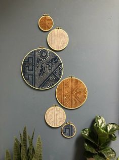 three handmade wall hangings on a gray wall next to a potted plant