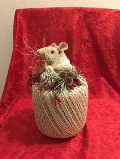 a white rat sitting on top of a red chair covered in pine cones and berries