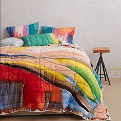 a bed with colorful comforter and pillows on it next to a small wooden table