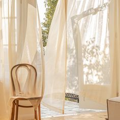 a chair sitting next to a window covered in sheer curtains