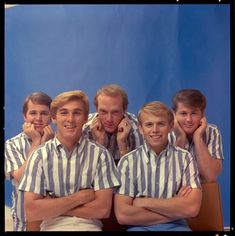 a group of men sitting next to each other in front of a blue wall with their arms crossed