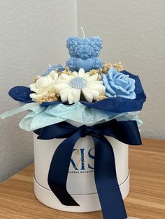 a blue teddy bear sitting on top of a white box filled with flowers and leaves