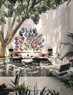 a living room filled with lots of furniture under a large tree next to a white wall