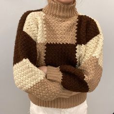 a woman wearing a brown and white sweater standing with her arms crossed in front of her chest