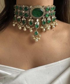 Inspired by the opulent designs of Sabyasachi, this emerald green Victorian choker set is the epitome of elegance and timeless beauty. The choker, meticulously crafted, features a central emerald stone surrounded by intricate gold filigree work that echoes the grandeur of the Victorian era. Each detail is a testament to the exquisite craftsmanship, with tiny pearls and delicate gold beads enhancing the necklace's regal appeal. Complementing the choker are a pair of matching earrings that mirror the necklace's luxurious design. The earrings feature a smaller version of the choker's central emerald, encircled by the same intricate gold detailing and pearls, offering a cohesive and sophisticated look. The emerald's deep green hue provides a striking contrast against the shimmering gold, creat Luxury Green Temple Jewelry Choker, Opulent Party Jewelry With Intricate Design, Elegant Kundan Jeweled Choker, Opulent Festive Party Jewelry, Elegant Green Kundan Necklace With Meenakari, Elegant Emerald Kundan Necklace With Stone Work, Elegant Kundan Necklace With Emerald Stone Work, Green Elegant Kundan Necklace For Party, Elegant Green Kundan Necklace For Party