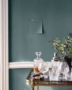 a table with vases and glasses on it in front of a wall painted teal