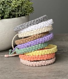 five crocheted headbands in different colors on a table next to a potted plant