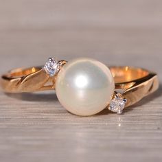 a pearl and diamond ring sitting on top of a wooden table