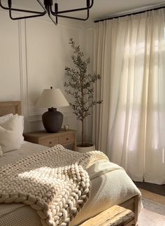 a bed sitting next to a window covered in white blankets and pillows on top of a wooden frame