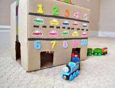 a cardboard box with cars and numbers on the inside is sitting on the floor next to a toy train