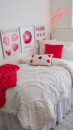 a bed with white sheets and red pillows in a room that has pictures on the wall