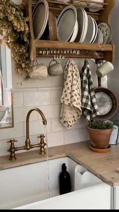 a kitchen sink with dishes hanging on the wall above it and a wooden shelf holding plates