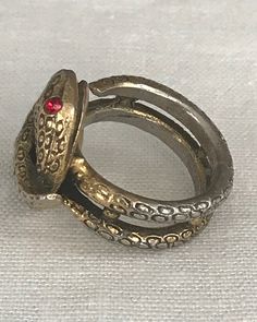 The two gold tone snakes with tiny red eyes are delicately wrapped around each other. The one snake has its body wrapped around the other one in the front of this ring and the second snake's body goes around and becomes the band of the ring and ends with the tip of its tale. This is a fun ring to wear. There are no markings on it. The double bands in the back of the ring are connected four tiny gold toned balls. This ring is in overall very good condition. Please see all photos and feel free to Adjustable Gold Metal Snake Ring, Adjustable Metal Snake Ring, Adjustable Symbolic Snake Ring, Antique Snake Ring As Gift, Symbolic Adjustable Snake Ring For Anniversary, Unique Adjustable Snake Ring For Anniversary, Adjustable Snake-shaped Symbolic Rings, Adjustable Snake Symbolic Ring, Adjustable Gold Snake Ring Symbolic