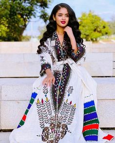 a woman is sitting on the steps wearing a white and multicolored dress with feathers