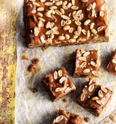 several pieces of brownie with nuts on top and one piece cut in half, sitting on parchment paper