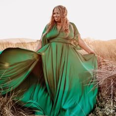 a woman in a long green dress standing in tall grass with her hands on her hips