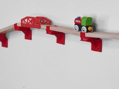 a toy train is on a track with red rails and wooden bridge over the tracks