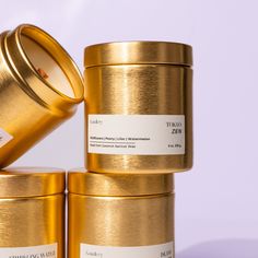 three gold tins stacked on top of each other, one containing a candle and the other containing a label